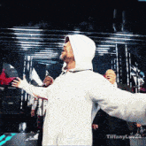 a man in a white hoodie stands on a stage with his arms outstretched and the words tiffanyluv24 below him