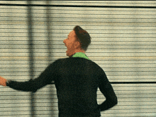 a man in a black sweater is standing in front of a striped wall with his mouth open