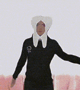 a person wearing a black sweater and a white collar is standing next to a pink couch .