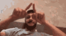 a man with a beard is making a peace sign with his hands in front of his eyes .