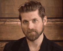 a man with a beard is wearing a black shirt and making a funny face .