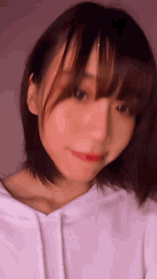 a woman with short hair and bangs is wearing a white hoodie and smiling .