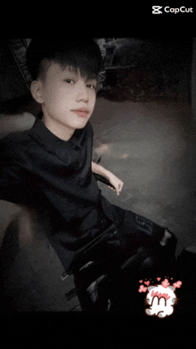 a boy in a black shirt is sitting in a chair with a capcut watermark on the bottom right