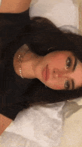 a woman wearing a black shirt and a pearl necklace is laying down on a bed