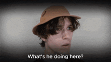 a man wearing a hat with the words what 's he doing here below him
