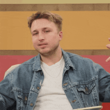 a man wearing a denim jacket and a white shirt looks at the camera