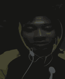 a man wearing headphones and a hooded jacket is looking at the camera in the dark .