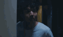 a man in a white t-shirt is standing in a dark room .