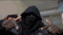 a man wearing a hooded jacket and a black mask is making a peace sign .