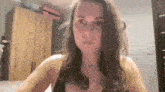 a woman in a black tank top is sitting in a bedroom looking at the camera .