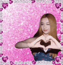 a girl is making a heart shape with her hands on a pink background .