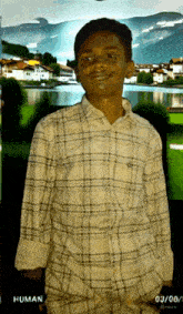 a young man in a plaid shirt stands in front of a picture of a lake and mountains