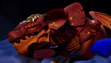 a red and gold dragon is laying down on a blue surface