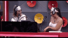 two women wearing headphones are sitting at a table with a laptop and a microphone .