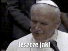 a man in a white robe is speaking into a microphone with the words jeszcze jak below him