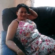 a woman in a floral dress is sitting on a couch with her hands on her head .