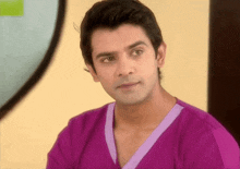a man in a purple shirt with a purple collar looks at the camera