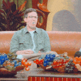 a man wearing glasses sits on a couch next to a bowl of berries