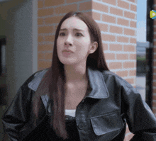 a woman wearing a black leather jacket stands in front of a brick building