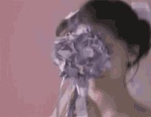 a woman in a wedding dress and veil is laughing and holding a bouquet of purple flowers .