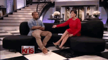 a woman in a red dress sits on a couch with a man in a blue shirt