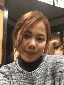 a woman wearing a grey sweater and a black turtleneck smiles for the camera