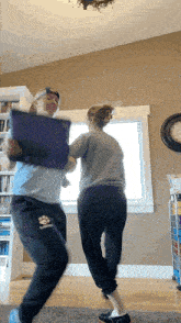 two women are dancing in a living room with one wearing a blue shirt with a paw print on it