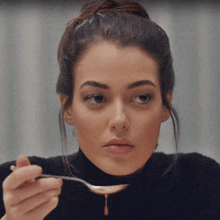 a woman in a black turtleneck is holding a spoon with liquid dripping out of it