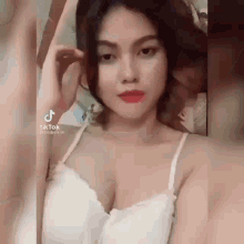 a woman in a white tank top is taking a selfie with her phone .