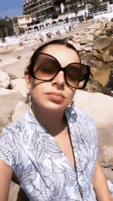 a woman wearing sunglasses and a blue shirt takes a selfie
