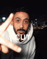 a man with a beard is making a peace sign and the word cut is visible behind him