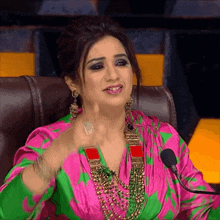 a woman in a pink and green dress speaking into a microphone