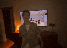 a man in a plaid shirt is standing in front of a television with a group of women dancing on it