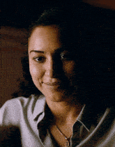 a woman wearing a white shirt and a gold necklace smiles for the camera
