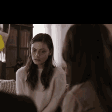 two women are sitting on a couch and talking to each other