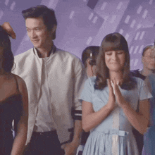 a woman in a blue dress is clapping while a man in a white jacket stands behind her