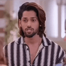 a man with long hair and a beard is wearing a black and white shirt and necklace .