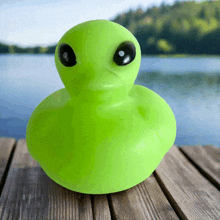 a green rubber duck with black eyes is on a wooden dock