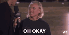 a woman is talking into a microphone and the words oh okay are visible