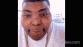 a close up of a man 's face with a white shirt and a chain around his neck .