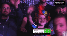 a young boy wearing a colorful mohawk stands in a crowd of people watching a game of darts
