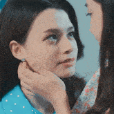 a woman wearing a blue shirt with white polka dots is touching the face of another woman