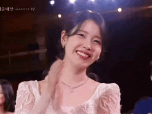 a woman in a white dress with a necklace and earrings is smiling