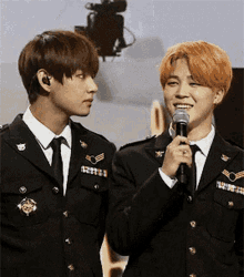 two young men in military uniforms are standing next to each other and one is holding a microphone