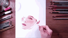 a person is drawing a woman 's face with colored pencils on a table