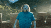 a man with a beard wearing a blue shirt is standing in front of mountains