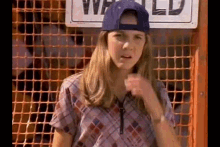 a young girl wearing a baseball cap and plaid shirt is standing in front of a fence .