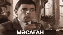 a man in a suit and tie is drinking from a cup with the word macafah written on the bottom