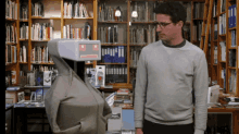 a man standing next to a robot in a library with bookshelves behind him