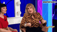 a woman in a red dress sits next to another woman in a chair on a television show with the number 3 on the screen behind them